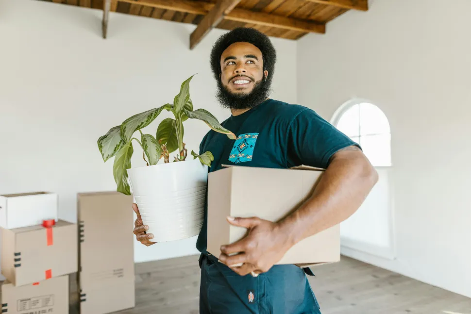 Hombre llevando planta y cartón